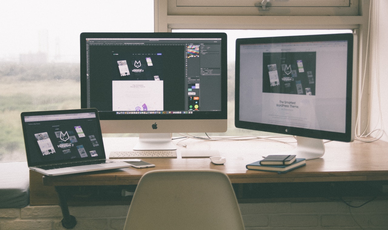 Styr merkevaren din med grafisk design. Foto av en pult med to skjermer og en Mac laptop.