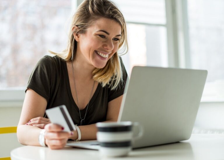 PPC - annonsering på nett foto. Bilde av en kvinne som smiler mot en laptop mens hun sitter med en kaffikopp og kredittkort i hånden.