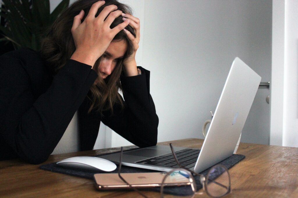 Frustrert kvinne holder hendene på hode mens hun stirrer på laptopen sin